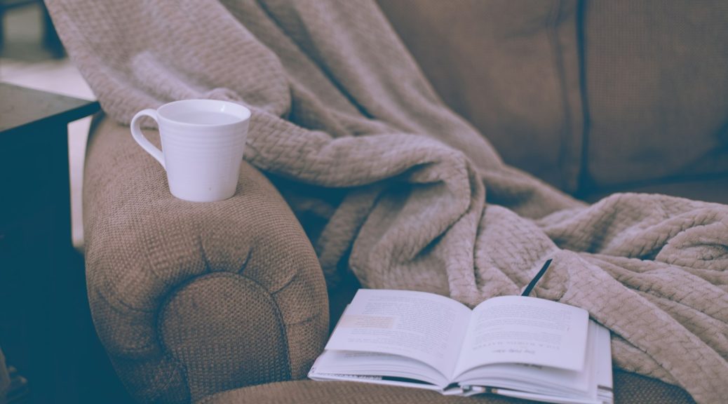 A mug and an open book on a blanket on the couch